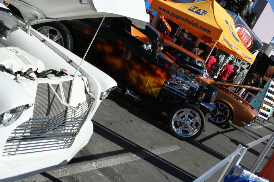 Hot rod with flame paint and chromed V8 next to a copper coupe at a car show