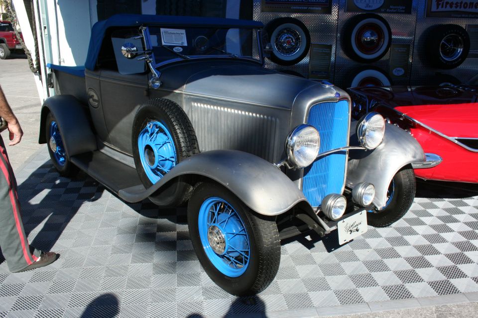 Bare-metal 1930s roadster hot rod with blue wire wheels on a checkered floor