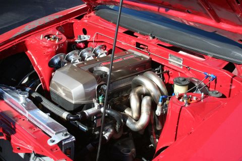 1998 Ford Crown Victoria - engine bay of a red car displays a polished twin-cam engine with velocity stacks and stainless headers under a raised hood.