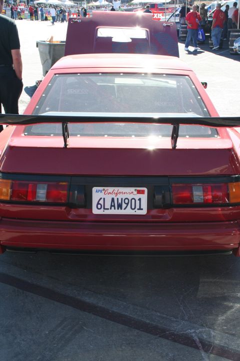 1998 Ford Crown Victoria - Rear view of a red sport coupe fitted with a large rear wing and California plate 6LAW901, parked at a crowded outdoor car event.