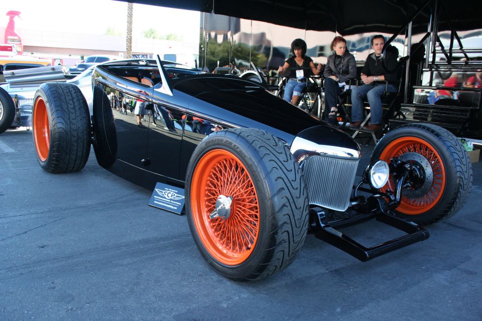 Black custom roadster hot rod with orange wire wheels and spectators at a show