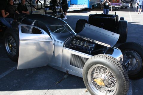 1998 Ford Crown Victoria - polished bare-aluminum streamlined hot rod sits at an outdoor show with its hood open, exposing a chrome-topped V8 and tall wire-spoke whee…