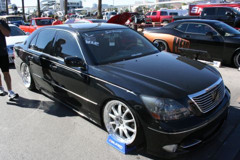 1998 Ford Crown Victoria - lowered black Lexus LS sedan on staggered white wheels sits among other vehicles at an outdoor car show.