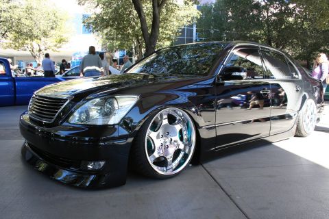 1998 Ford Crown Victoria - deep-gloss black Lexus LS sedan sits slammed on polished chrome multi-spoke wheels on a shaded show ground.