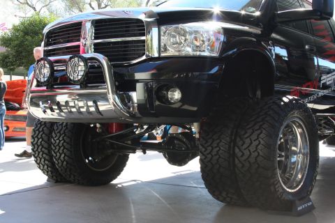 1998 Ford Crown Victoria - Low front-corner view of a lifted black Dodge Ram showing the chrome brush guard, round KC driving lights, and exposed suspension.