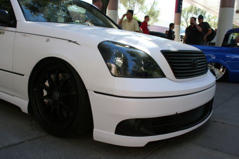 1998 Ford Crown Victoria - Low front-corner view of a white Lexus LS sedan on black wheels with a smoked headlight and blacked-out grille.