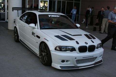 1998 Ford Crown Victoria - white BMW M3 coupe with a vented hood, front splitter, bronze wheels and a rear wing parked outside a building.