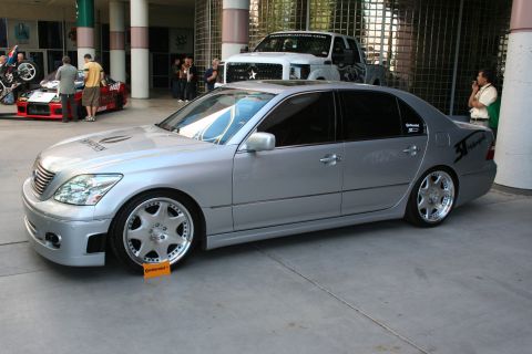 1998 Ford Crown Victoria - silver Lexus LS sedan sits lowered on polished multi-spoke wheels under a covered show area with a truck behind it.