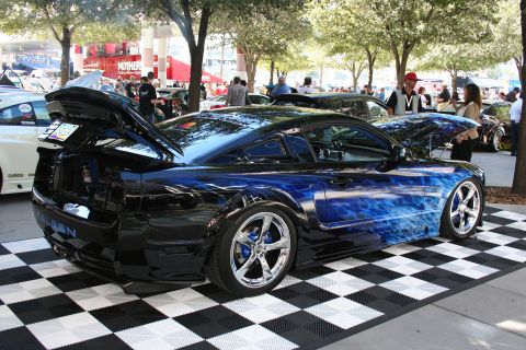 1998 Ford Crown Victoria - Rear three-quarter view of a black Ford Mustang with blue flame airbrushing and chrome wheels on a checkered show floor.