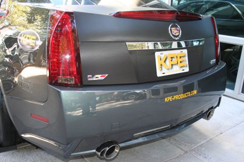 1998 Ford Crown Victoria - Close rear view of a gray Cadillac CTS-V showing the V badge, carbon-fiber trunk panel, dual exhaust and a yellow KPE license plate.