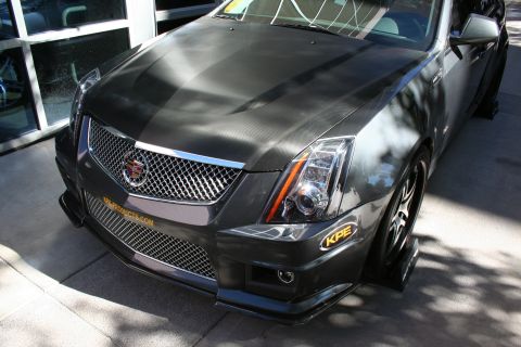 1998 Ford Crown Victoria - Front-corner view of a gray Cadillac CTS-V coupe showing the chrome mesh grille, projector headlight and a KPE splitter.