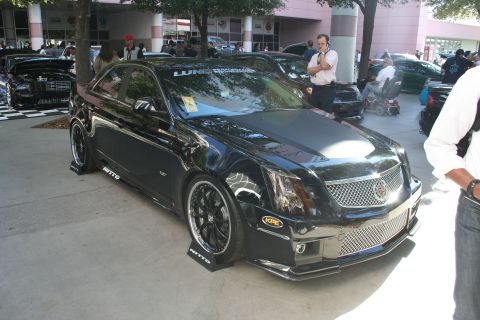 1998 Ford Crown Victoria - Front three-quarter view of a black Cadillac CTS-V sedan on black wheels with splitters at a busy outdoor car show.