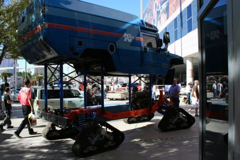 1998 Ford Crown Victoria - blue boxy SUV body is raised on a tracked all-terrain chassis as an elevated K&N branded display outside a building.