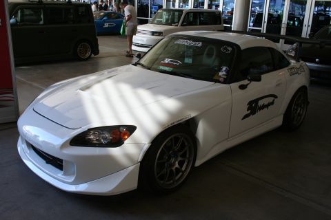 1998 Ford Crown Victoria - white Honda S2000 roadster fitted with a hardtop and sponsor decals sits under a covered area at a car show.