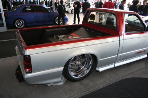 1998 Ford Crown Victoria - Rear three-quarter view of a lowered silver custom pickup with a red pinstriped bed rail and polished five-spoke wheels at an indoor show.