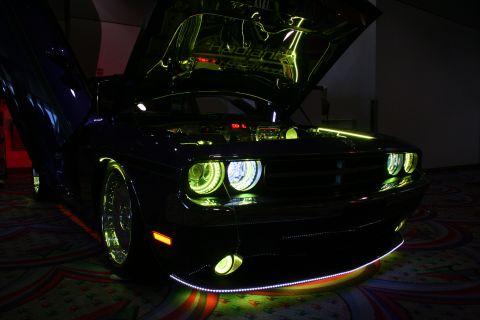 1998 Ford Crown Victoria - dark Dodge Challenger lit with green halo headlights, engine-bay and underbody LED glow, displayed in a dimly lit hall.