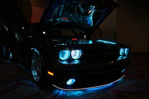 1998 Ford Crown Victoria - dark Dodge Challenger illuminated with blue and teal halo headlights and underbody LED lighting, hood raised in a dark room.