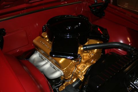 1998 Ford Crown Victoria - Close-up of a gold-painted V8 engine block topped with a black oval air cleaner inside the red engine bay of a classic car.