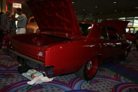 1998 Ford Crown Victoria - Rear three-quarter view of a lowered dark red classic coupe with its trunk open on patterned convention carpet, spectators nearby.