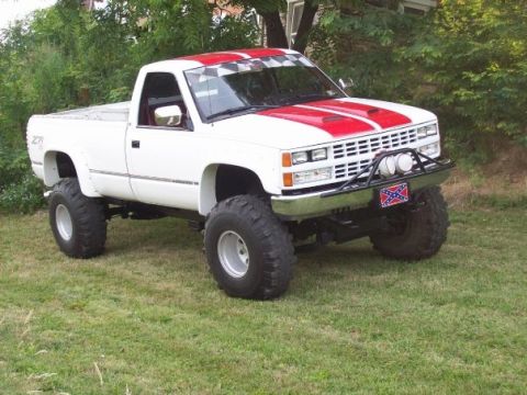 1988 Chevrolet C/K Pickup - This lifted pickup truck features a white body with red racing stripes and a checkered flag decal on the windshield.