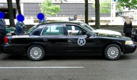 1991 Ford Crown Victoria - A black U.S. Marshal sedan is parked on the street, showing its side profile and official markings.