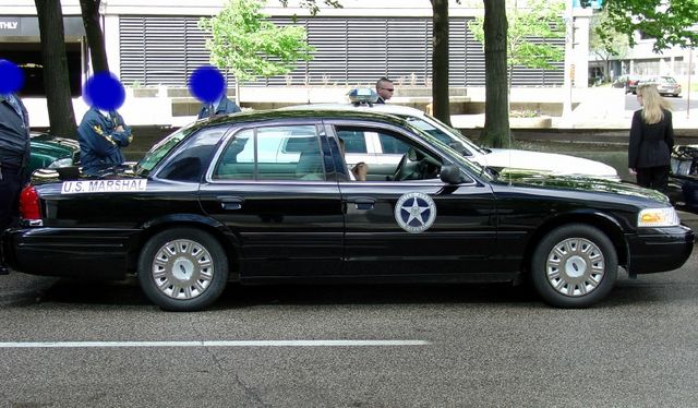 Black Ford Crown Victoria U.S. Marshal police sedan parked curbside, side view
