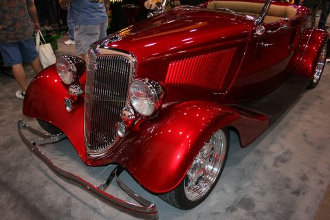 1998 Ford Crown Victoria - Front-quarter view of a candy-red vintage roadster hot rod with a chrome grille, dual headlights, bumper bars and polished wheels at a show.