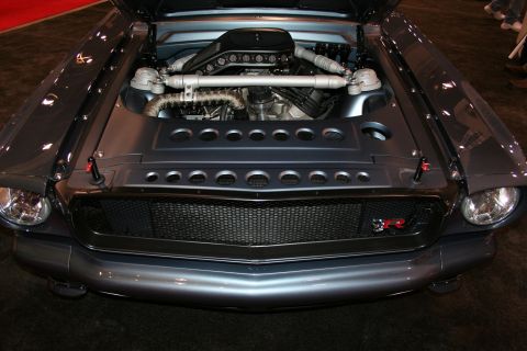 1998 Ford Crown Victoria - Open hood of a grey muscle car revealing a twin-turbo V engine with polished intercooler piping and a louvered cover, headlights flanking t…