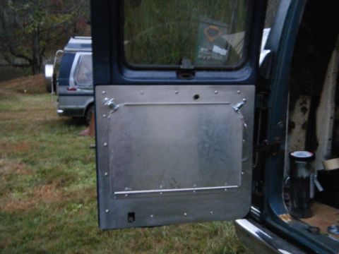 1981 Ford E350 - The interior of a van door is shown, with a metal panel installed. Another van is visible in the background.