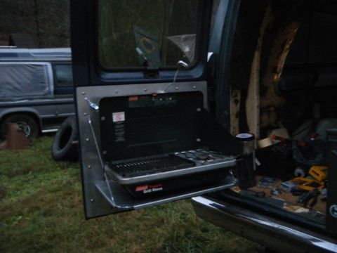 1981 Ford E350 - A portable grill stove is mounted to the side of a van, with another vehicle visible in the background.