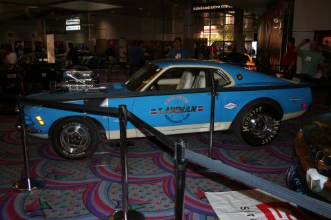 1998 Ford Crown Victoria - blue-and-white vintage muscle car with a tall chromed blower through the hood and 'Lawman' lettering on the door, roped off at an indoor ex…