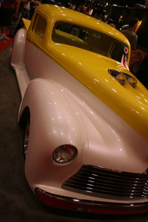 1998 Ford Crown Victoria - Low front-quarter view of a chopped two-tone yellow-and-white custom car with a horizontal-bar chrome grille and small headlight at a show.