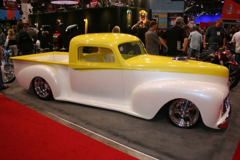 1998 Ford Crown Victoria - lowered custom pickup truck with a yellow upper body, white lower body, and chrome wheels displayed at an indoor automotive show.