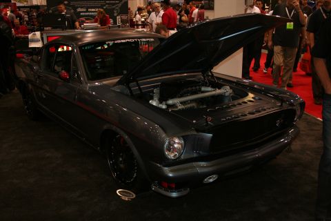 1998 Ford Crown Victoria - Front three-quarter view of a dark gray custom fastback muscle car with raised hood revealing the engine at a show.