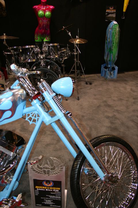 1998 Ford Crown Victoria - light-blue custom chopper motorcycle with spiderweb tank graphics displayed near a drum kit in a show booth.