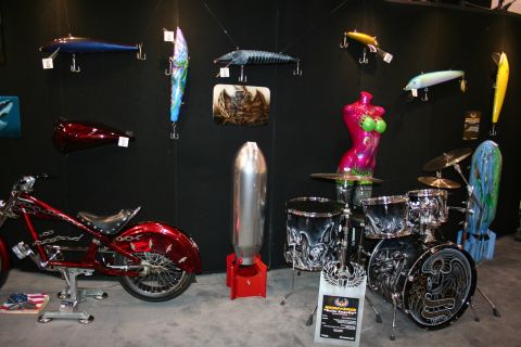 1998 Ford Crown Victoria - vendor booth displaying airbrushed fishing lures, a custom-painted drum kit, mannequin, and a red custom motorcycle.