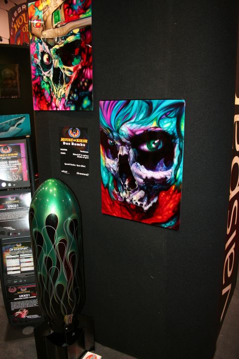1998 Ford Crown Victoria - colorful airbrushed skull painting mounted on a black booth wall beside a green flame-painted board and signage.