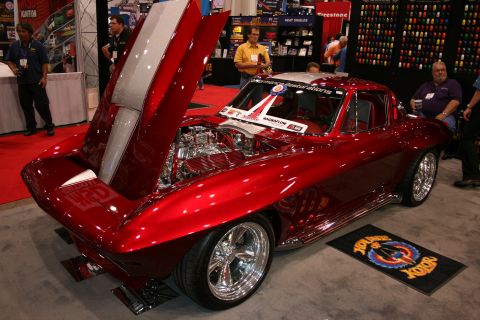 1998 Ford Crown Victoria - candy-red custom 1960s-style sports coupe with chrome wheels and open hood displayed at an indoor show.