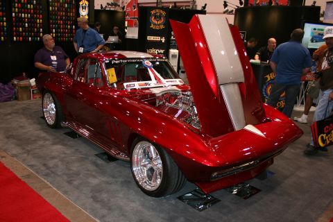1998 Ford Crown Victoria - candy-red custom split-window coupe with its front clip tilted up to show the engine, on display at a show booth.