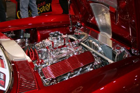 1998 Ford Crown Victoria - Engine bay of a candy-red custom car showing a heavily chromed V8 with a red finned valve cover.