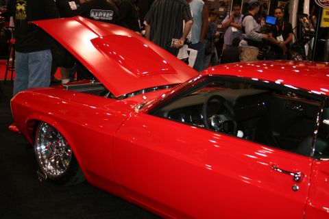 1998 Ford Crown Victoria - bright red custom fastback car with its hood raised and polished chrome wheels displayed in a crowded show hall.