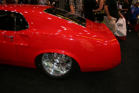 1998 Ford Crown Victoria - Side rear-quarter view of a bright red custom fastback car with a polished chrome five-spoke wheel.