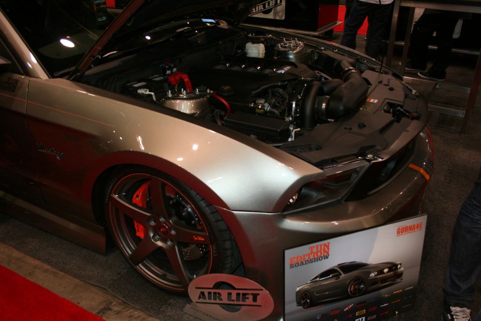 Silver-grey Mustang with open hood and Air Lift display board at indoor show