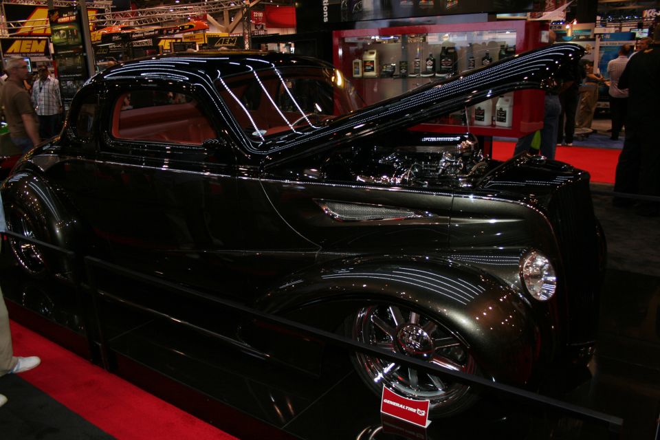 Black 1937-style hot rod coupe side profile with open hood on red carpet