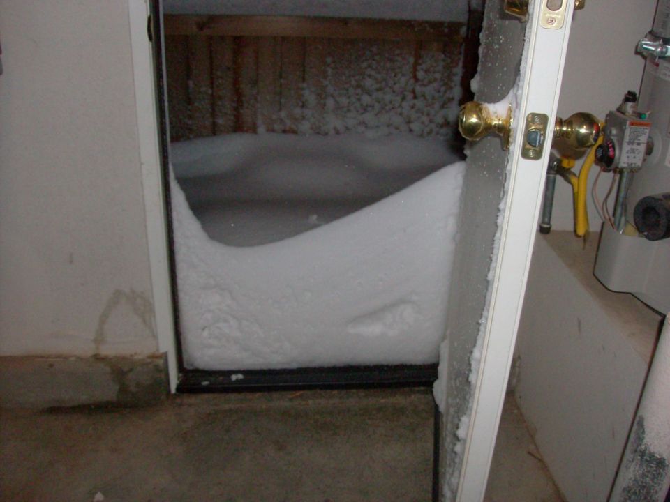 Snowdrift blocking a doorway, with a water heater and pipes visible to the right