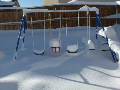 1995 Ford Bronco - A backyard swing set is buried under a thick blanket of snow, with only the blue frame and some of the seats visible.