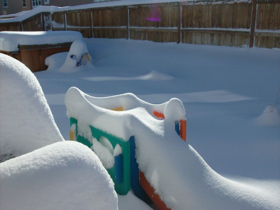 Backyard covered in deep snow, with a colorful plastic slide and mounds of snow obscuring other objects