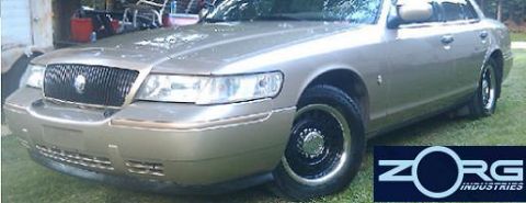 2000 Mercury Grand Marquis - A gold 2000 Mercury Grand Marquis is shown from the front 3/4 angle, parked outdoors on a grassy area.