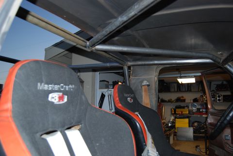 1982 Ford Bronco - Interior of a vehicle modified with racing seats and a roll cage, with a workshop visible in the background.