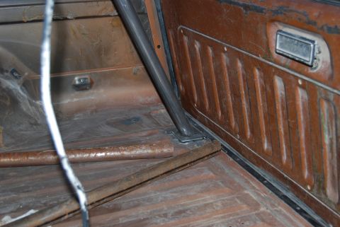 1982 Ford Bronco - The interior of a vehicle shows a roll cage and brown paneling, with a rusted floor.